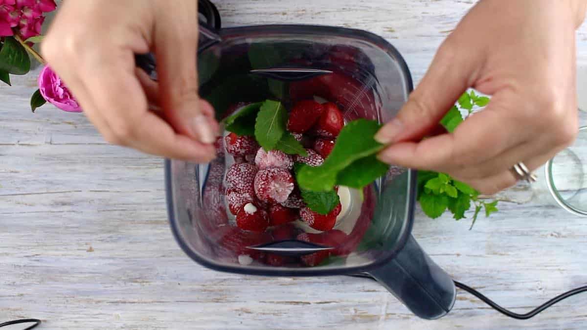 The Best Strawberry Keto Smoothie adding fresh mint leaves