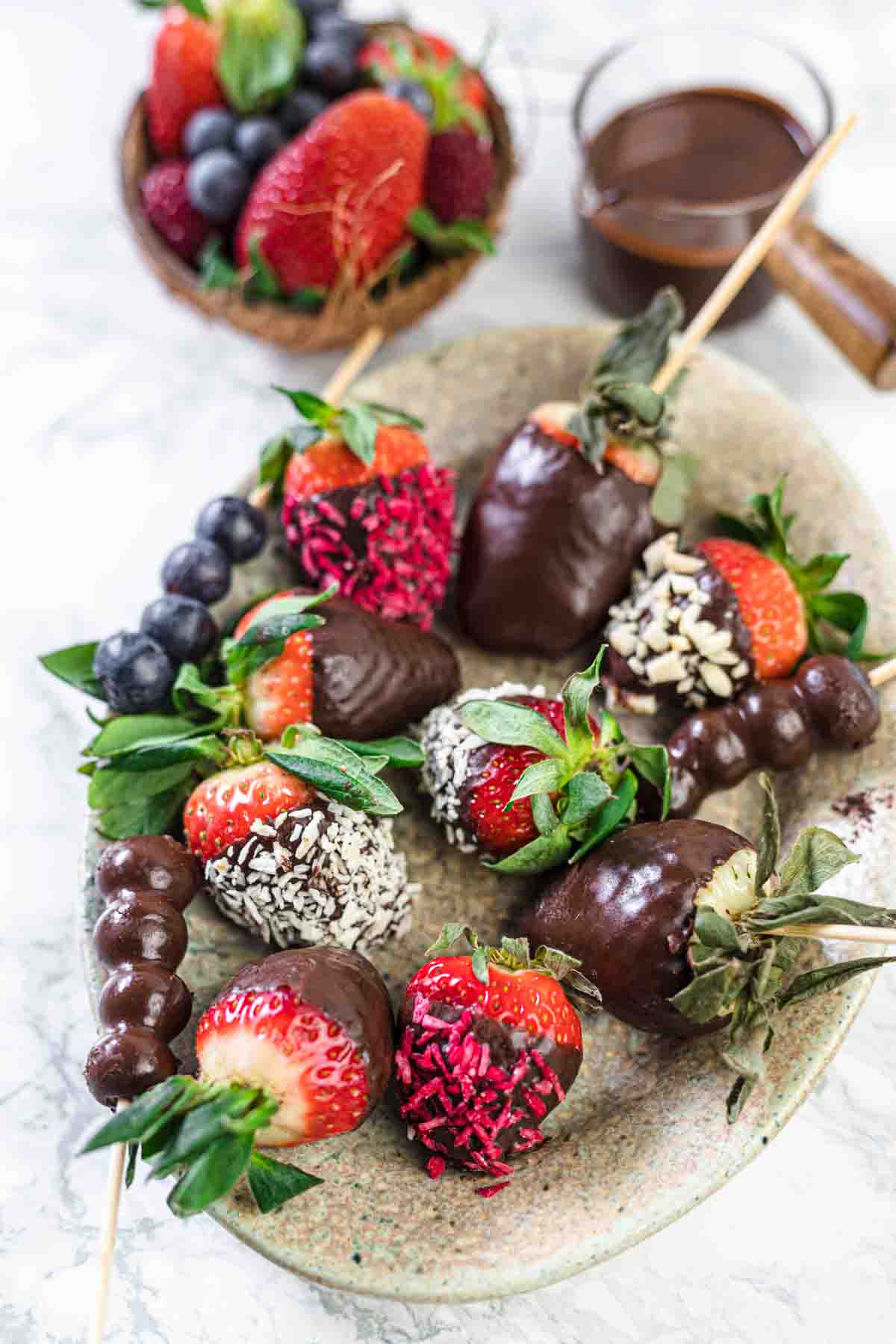 How To Make Chocolate Covered Strawberries on a plate covered with nuts, coconut and sprinkles