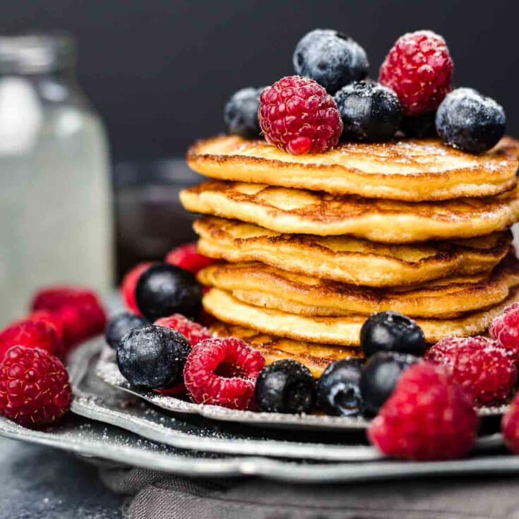 Low-Carb Pancakes stuck on top of each other with berries and powdered sugar.