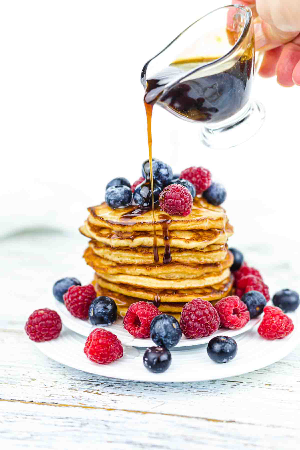 Low-Carb Pancakes with berries on the white table with poring syrup.