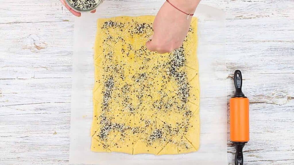 Keto Friendly Crackers sprinkling seeds over the dough..