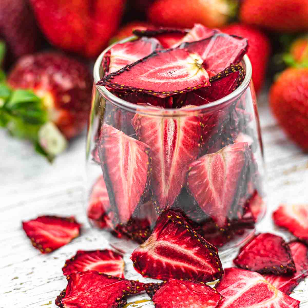 Dried Strawberries in a glass with fresh strawberries in the background.