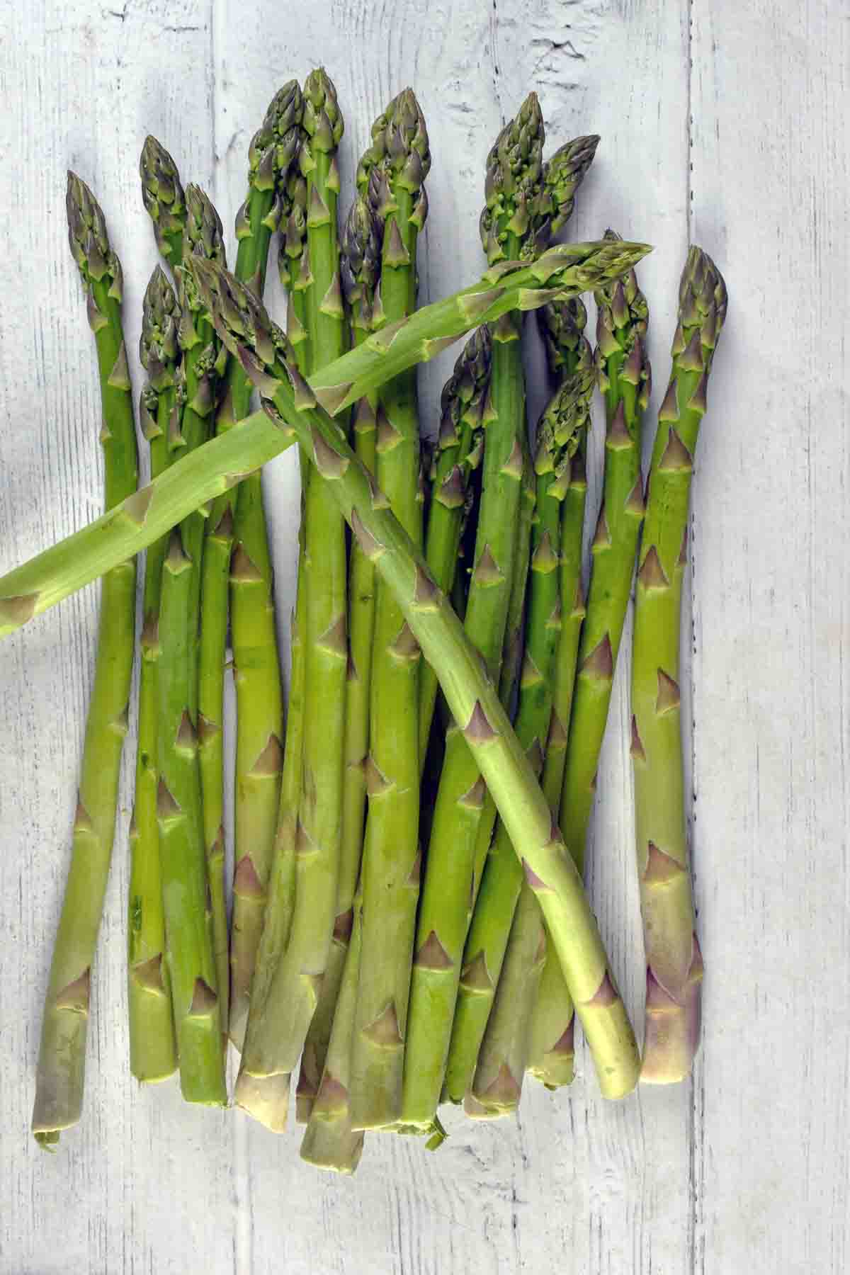 Fresh asparagus sticks on a white wooden board.