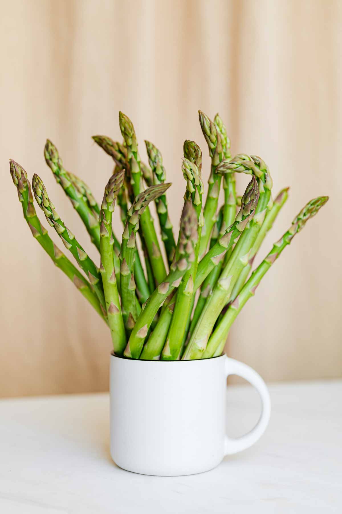 Fresh asparagus pieces in a white mug.
