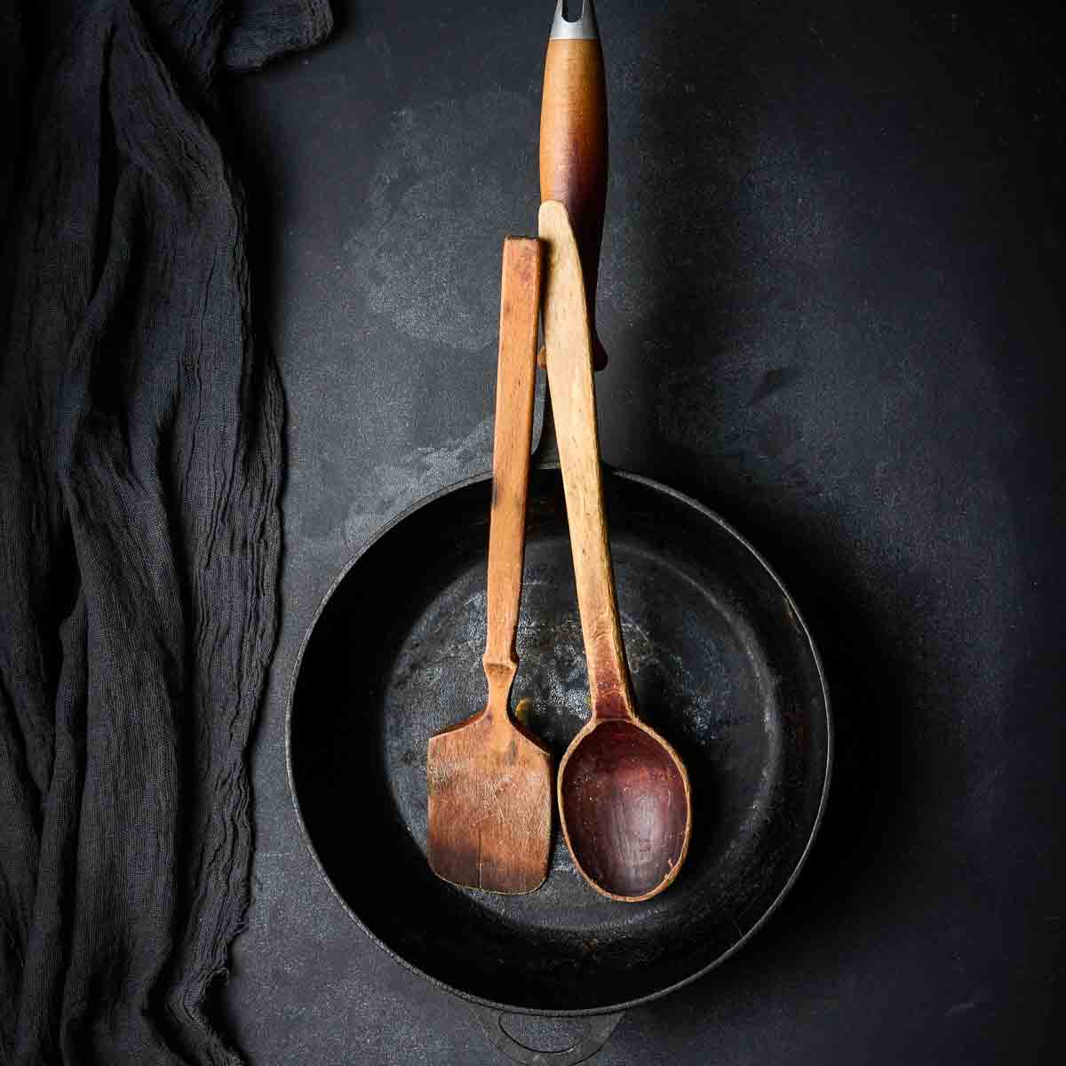 Empty round cast iron frying pan with wooden handle on black table.