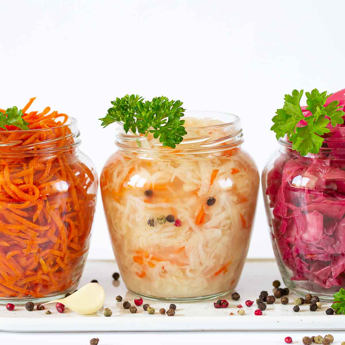 Sauerkraut, marinated red cabbage and carrot in open glass jars on ceramic board.