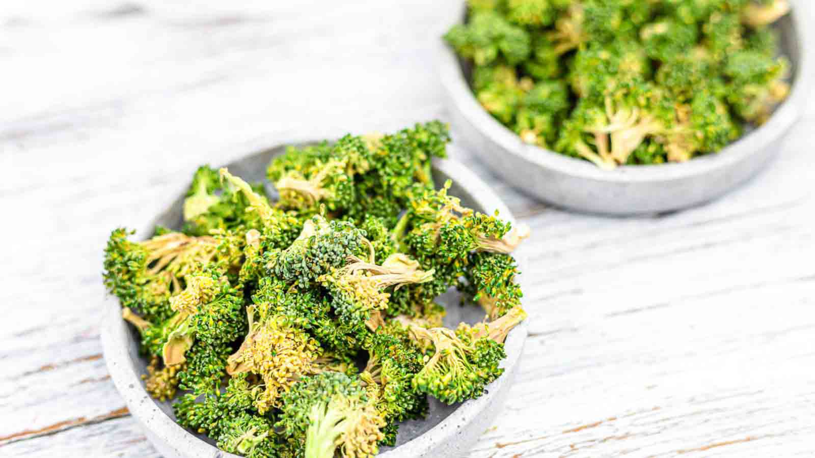 Two bowls of broccoli chips on a wooden table.