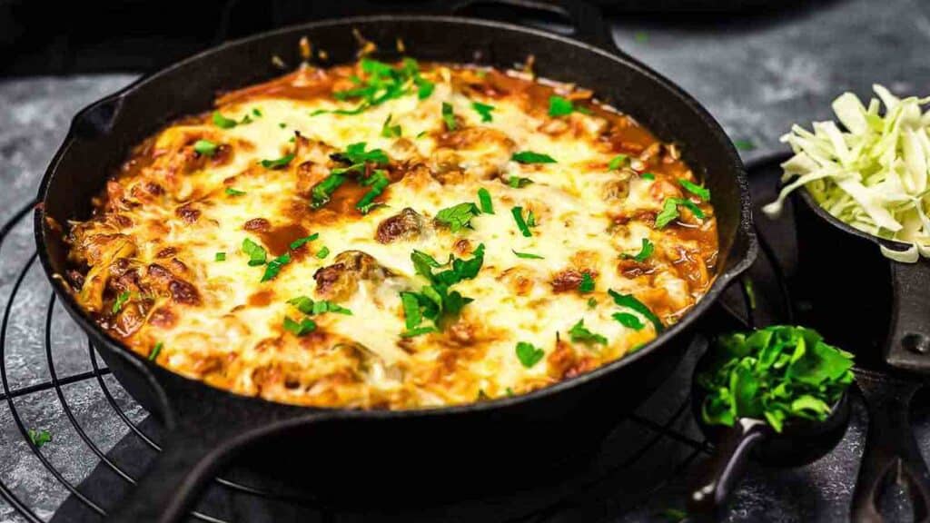 A skillet full of meat, cabbage and cheese on a table.