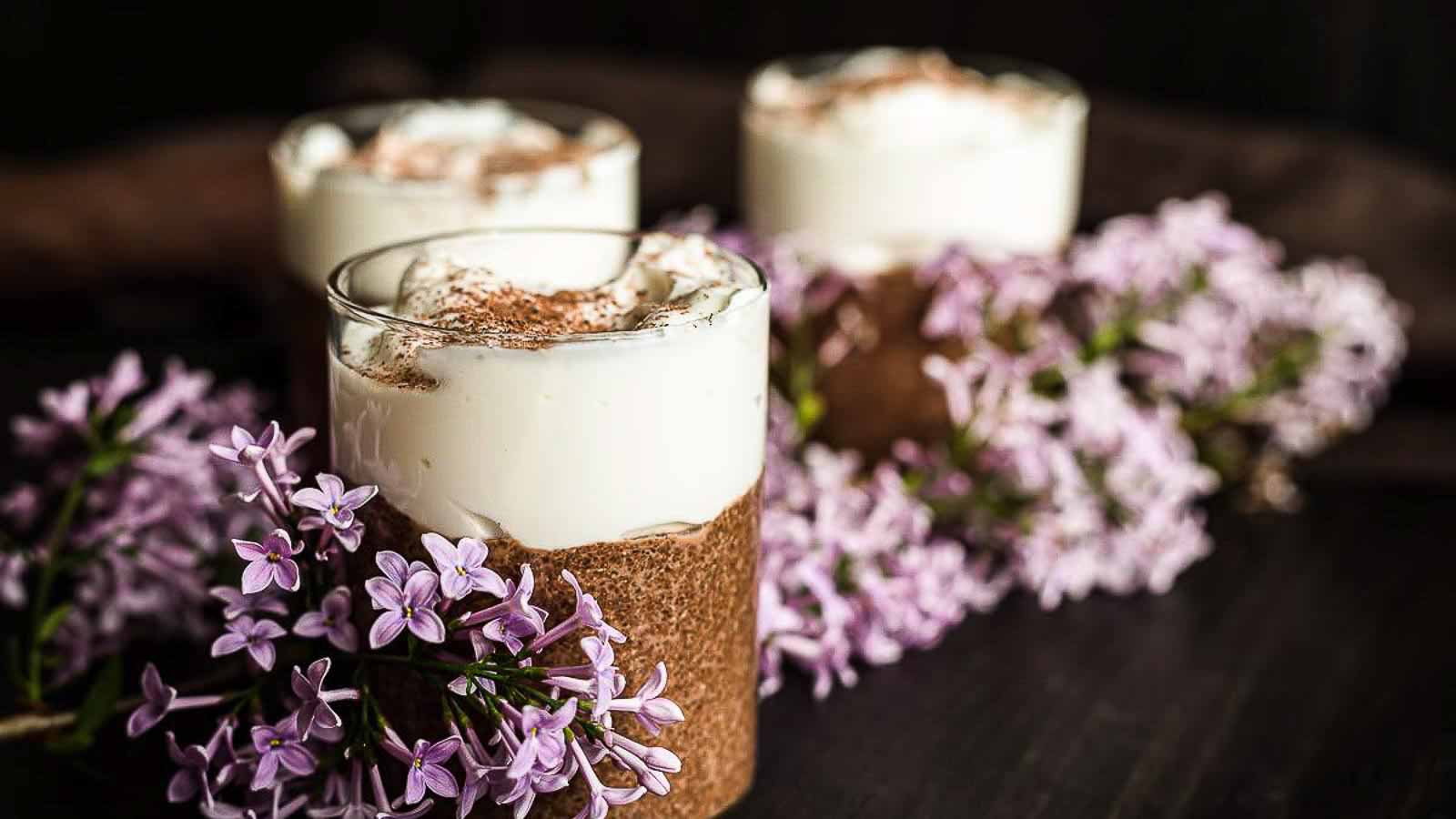 Three glasses with chia pudding, whipped cream and purple flowers.