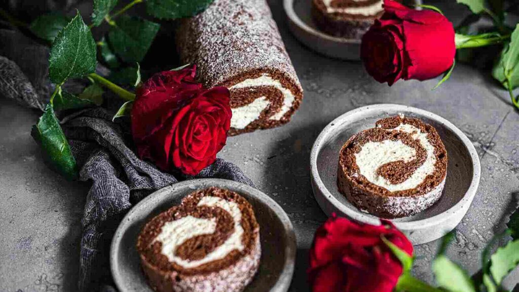 A chocolate roll with cream and roses on a table.