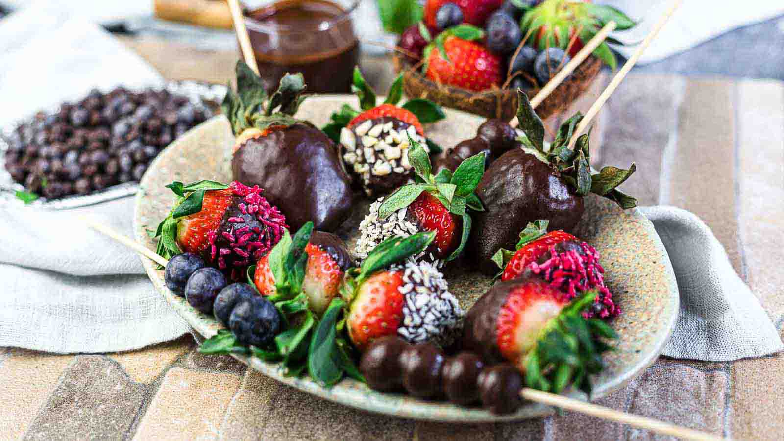 Chocolate covered strawberries on skewers on a plate.