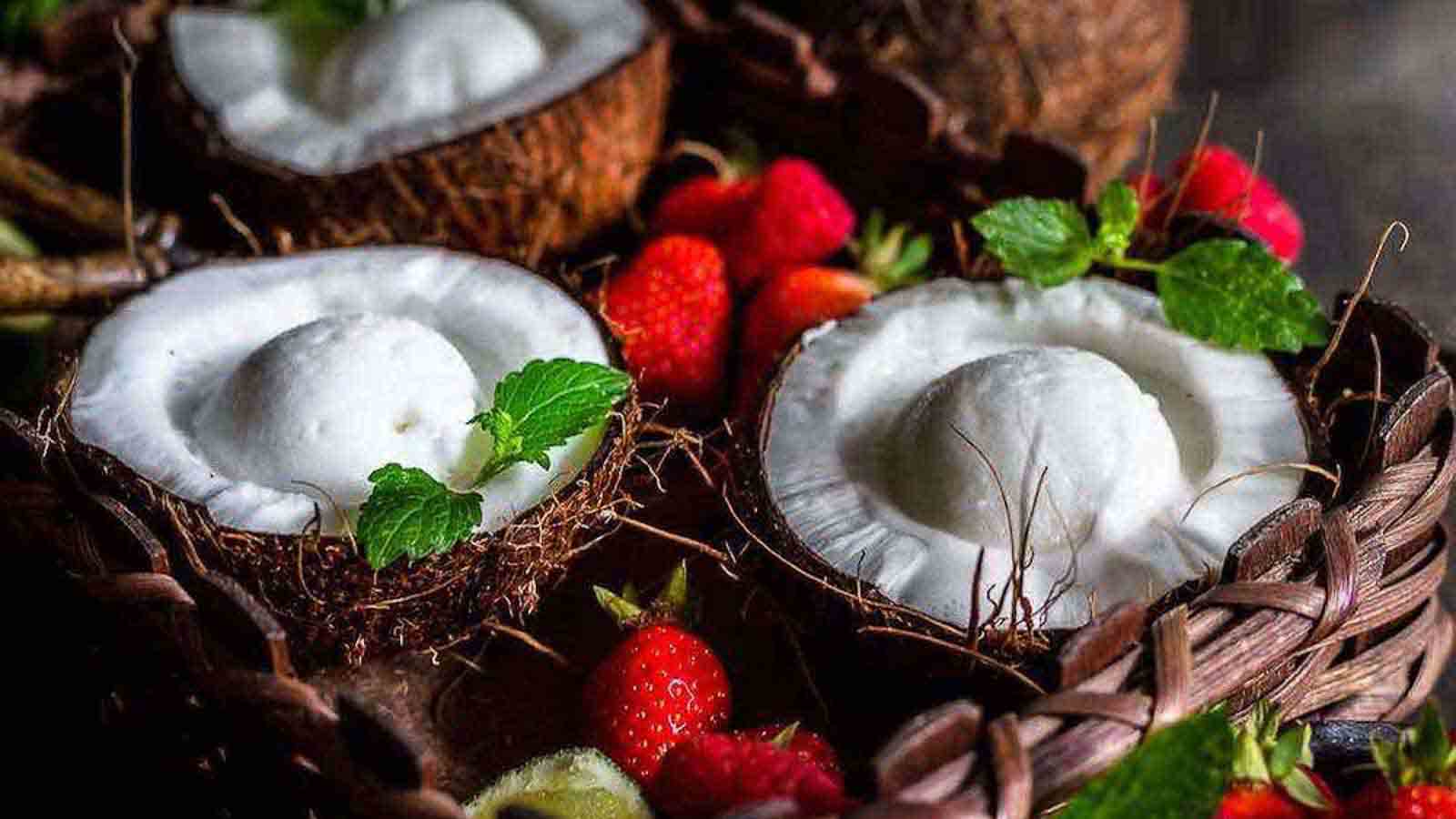 Two coconuts filled with ice cream and strawberries.