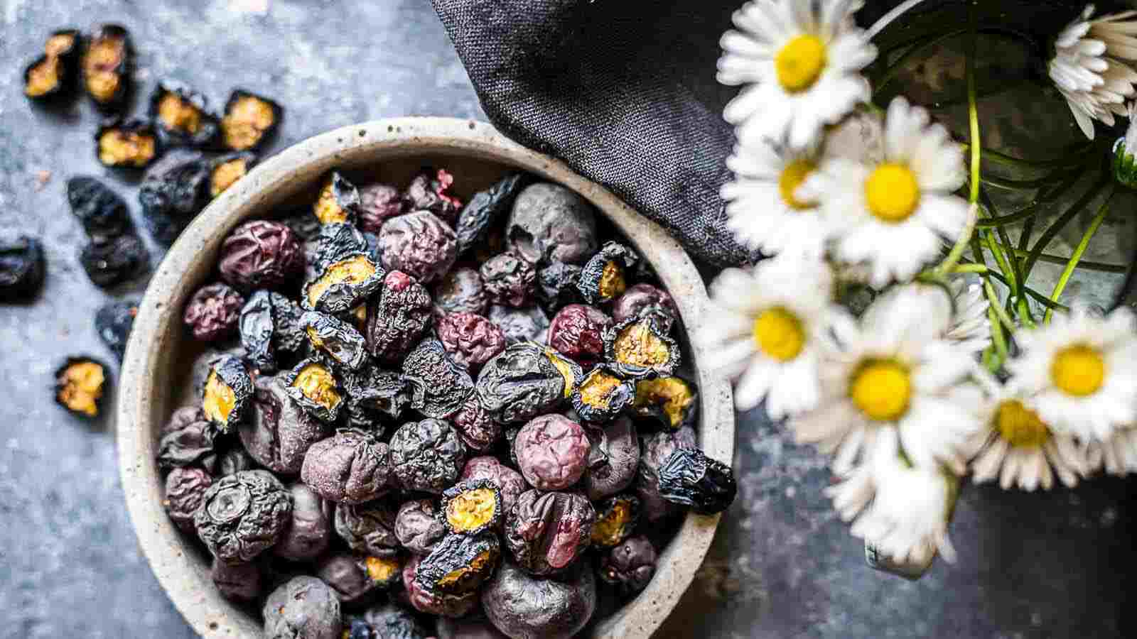 Dried blueberries in a bowl next to daisies.