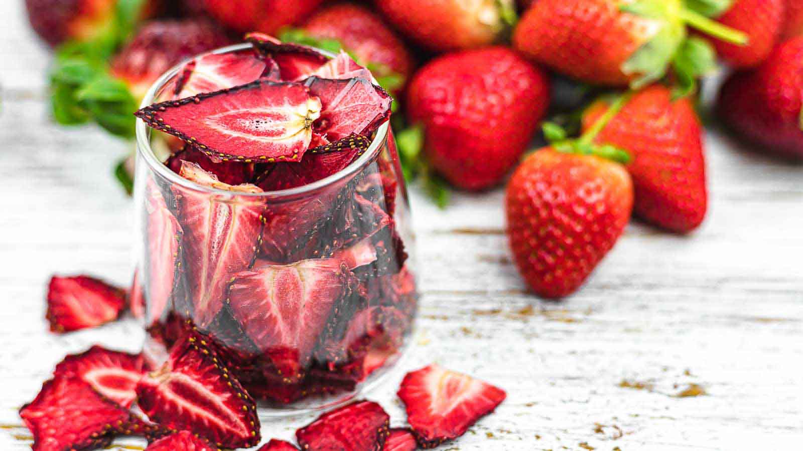 Dehydrated Strawberries in a glass with fresh strawberries in the background.
