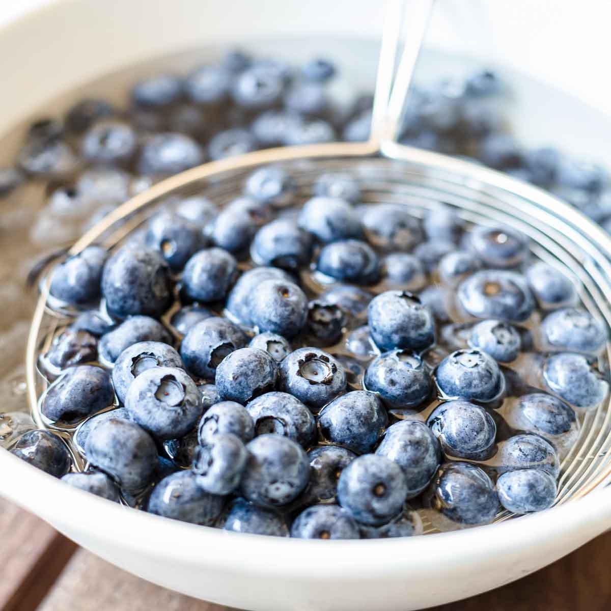 Blueberries in a white bowl on a wooden table.