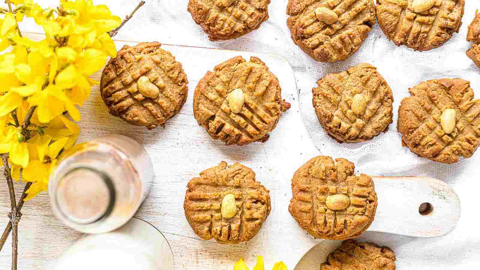 Peanut Butter Keto Cookies layered on a white surface with yellow flowers on the side.