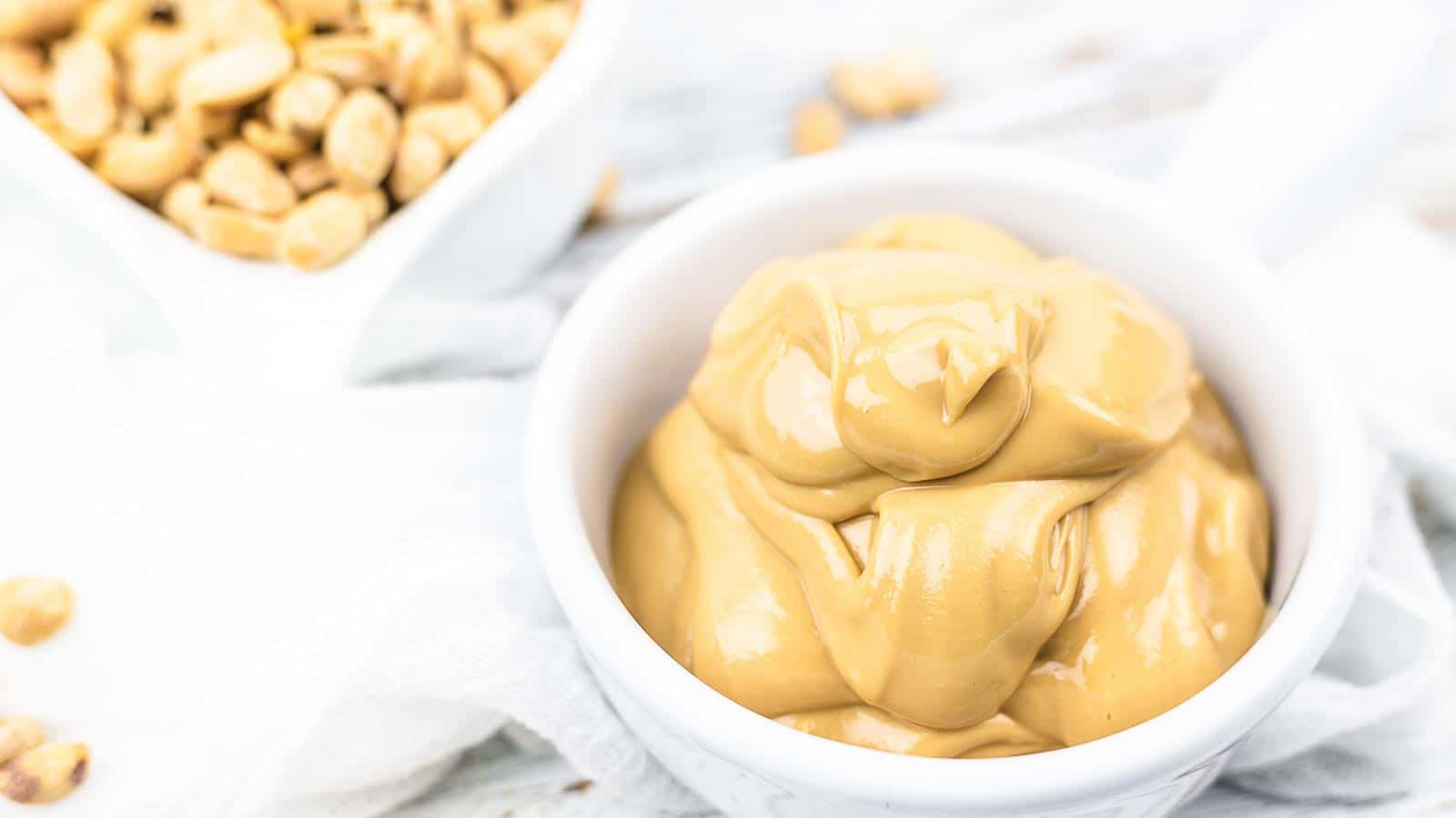 Peanut butter in a bowl next to peanuts.
