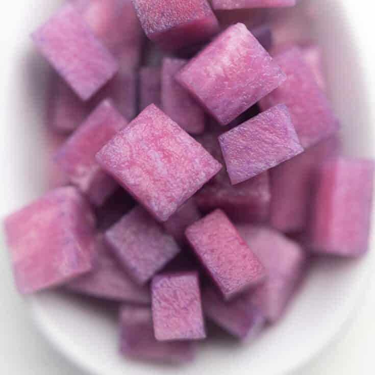 Purple cubes in a bowl on a white surface.
