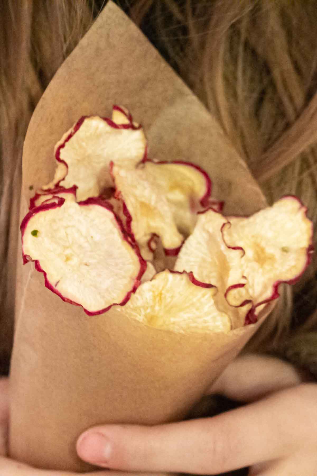 A girl holding a paper bag with sliced radishes in it.