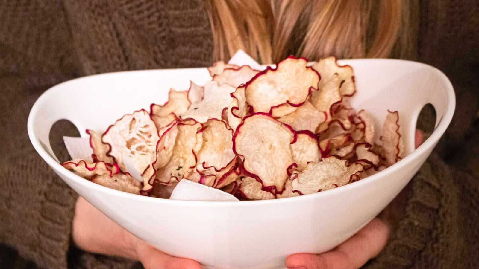 A girl holding a bowl of sliced radish chips.