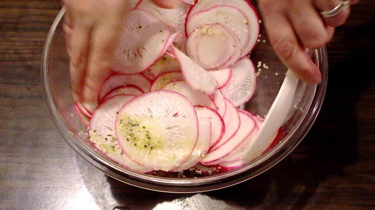 A person mixing radishes in a bowl.
