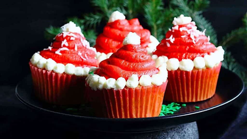 Four red santa hat cupcakes on a black plate.