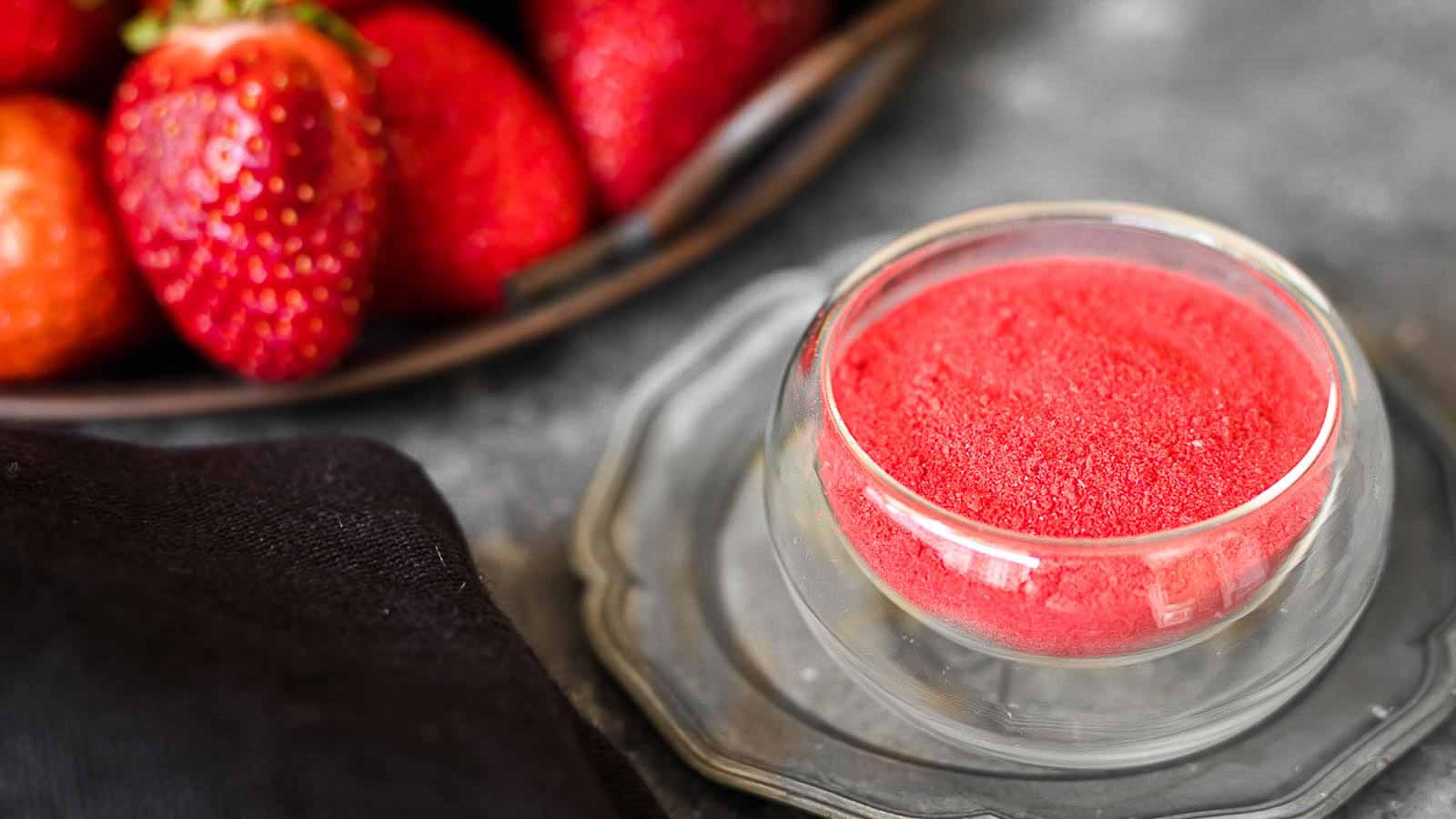 Strawberry Powder in a glass bowl with fresh strawberries behind.