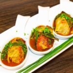 Three bowls of cabbage rolls with sauce on a white plate.