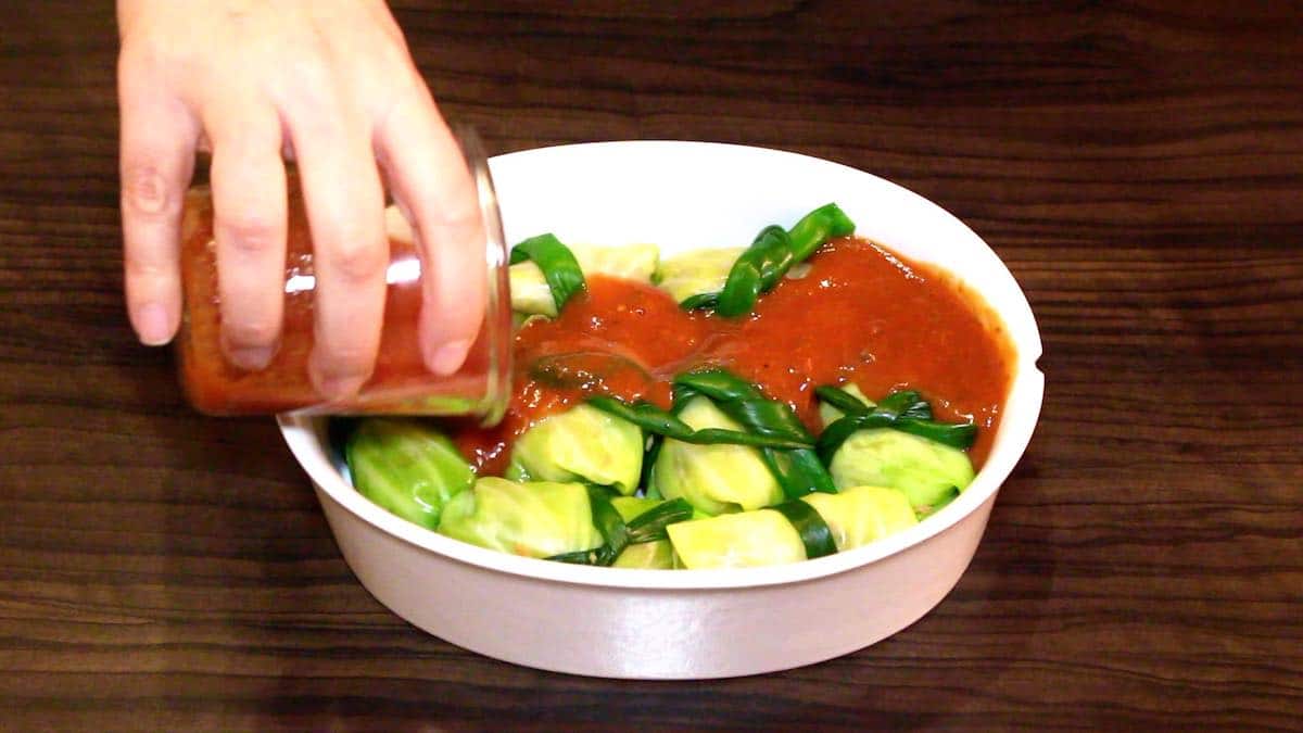 A person pouring sauce on a bowl of vegetables.