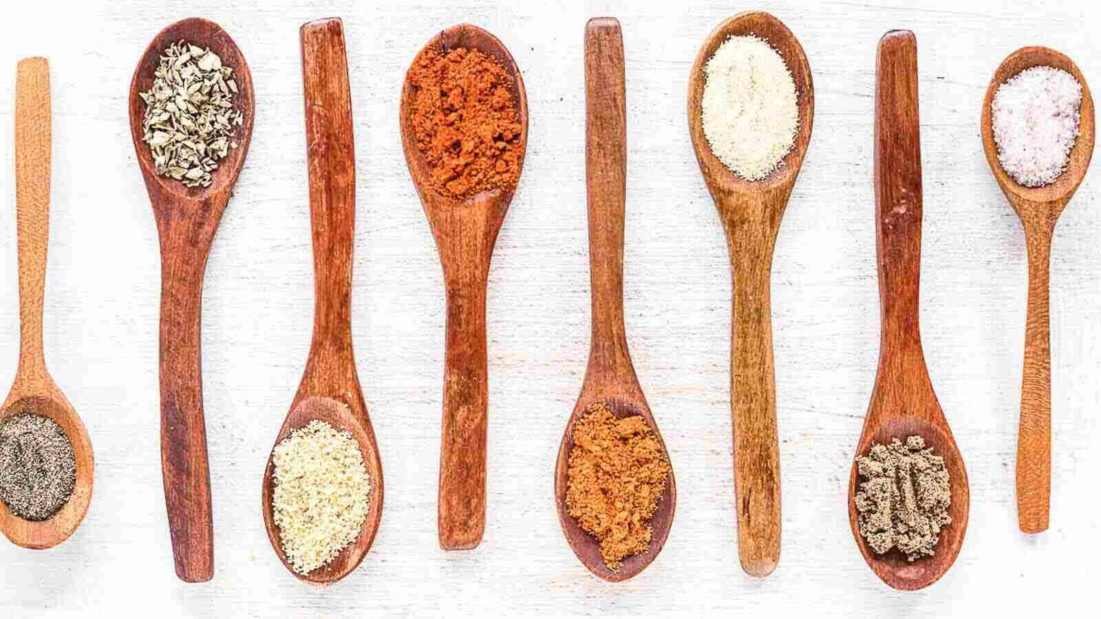 Spices in wooden spoons on a white background.
