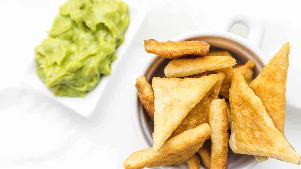 Guacamole and tortilla chips in a white bowl.