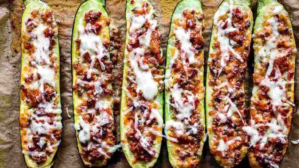Zucchini boats with cheese and bacon on a baking sheet.