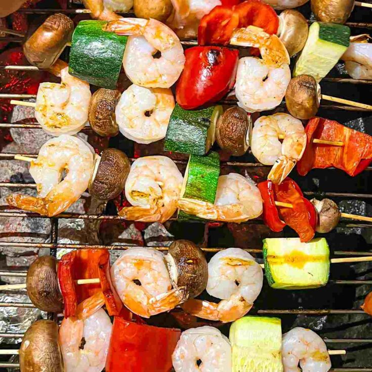 Shrimp and vegetables on skewers on a grill.
