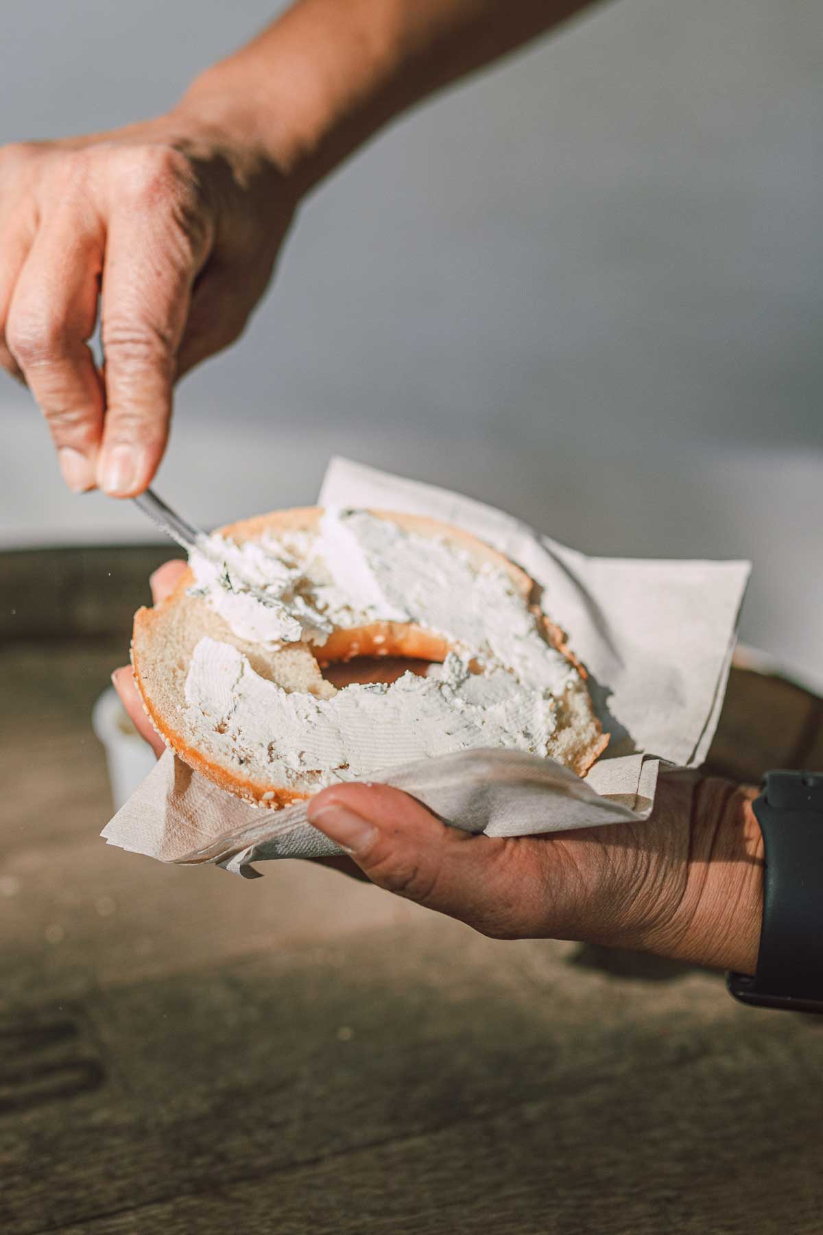 A person spreading cream cheese on a bagel.