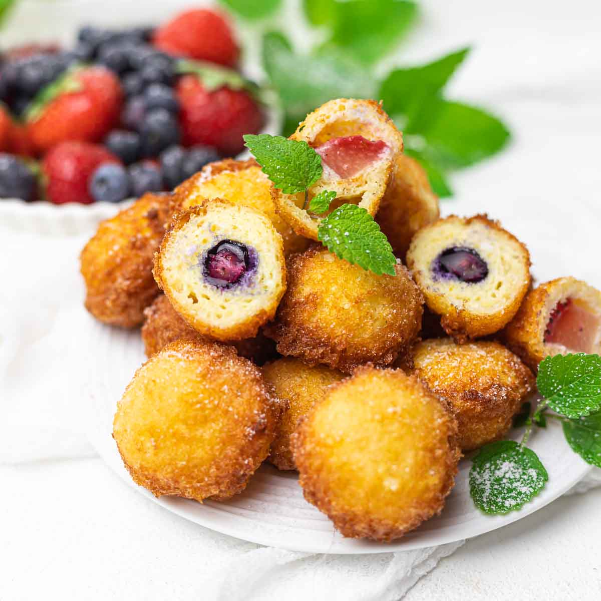 A plate of fried cheesecake bites with strawberries and blueberries.
