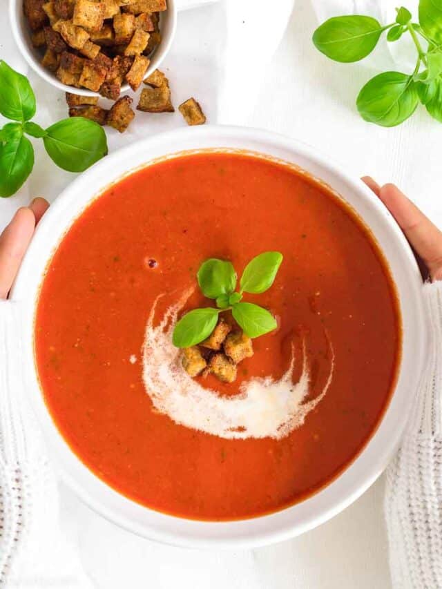 A bowl of tomato soup with croutons and basil.