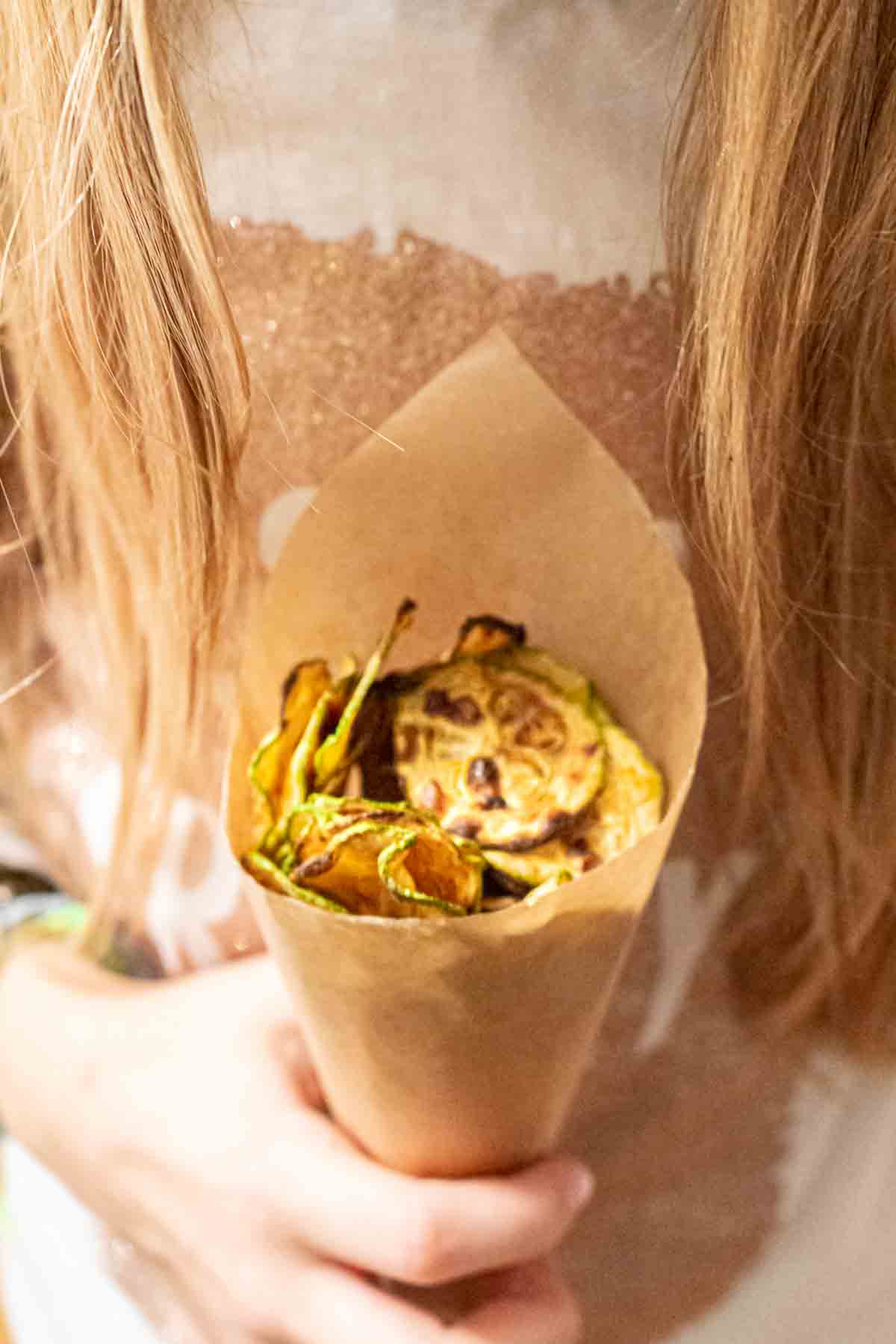 A girl holding a brown paper bag filled with chips.