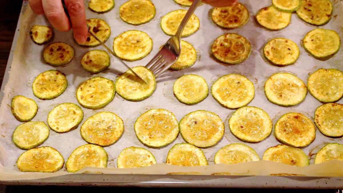 Zucchini slices on a baking sheet with a fork.