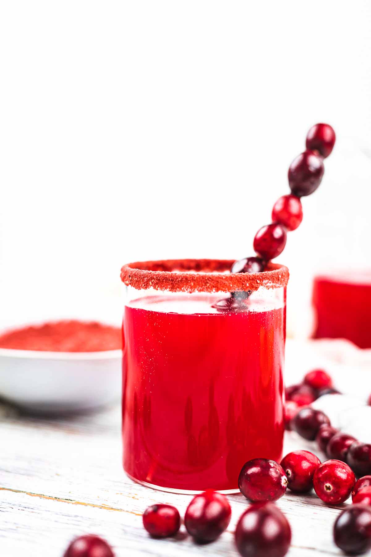 A glass of cranberry juice with a straw surrounded by cranberries.