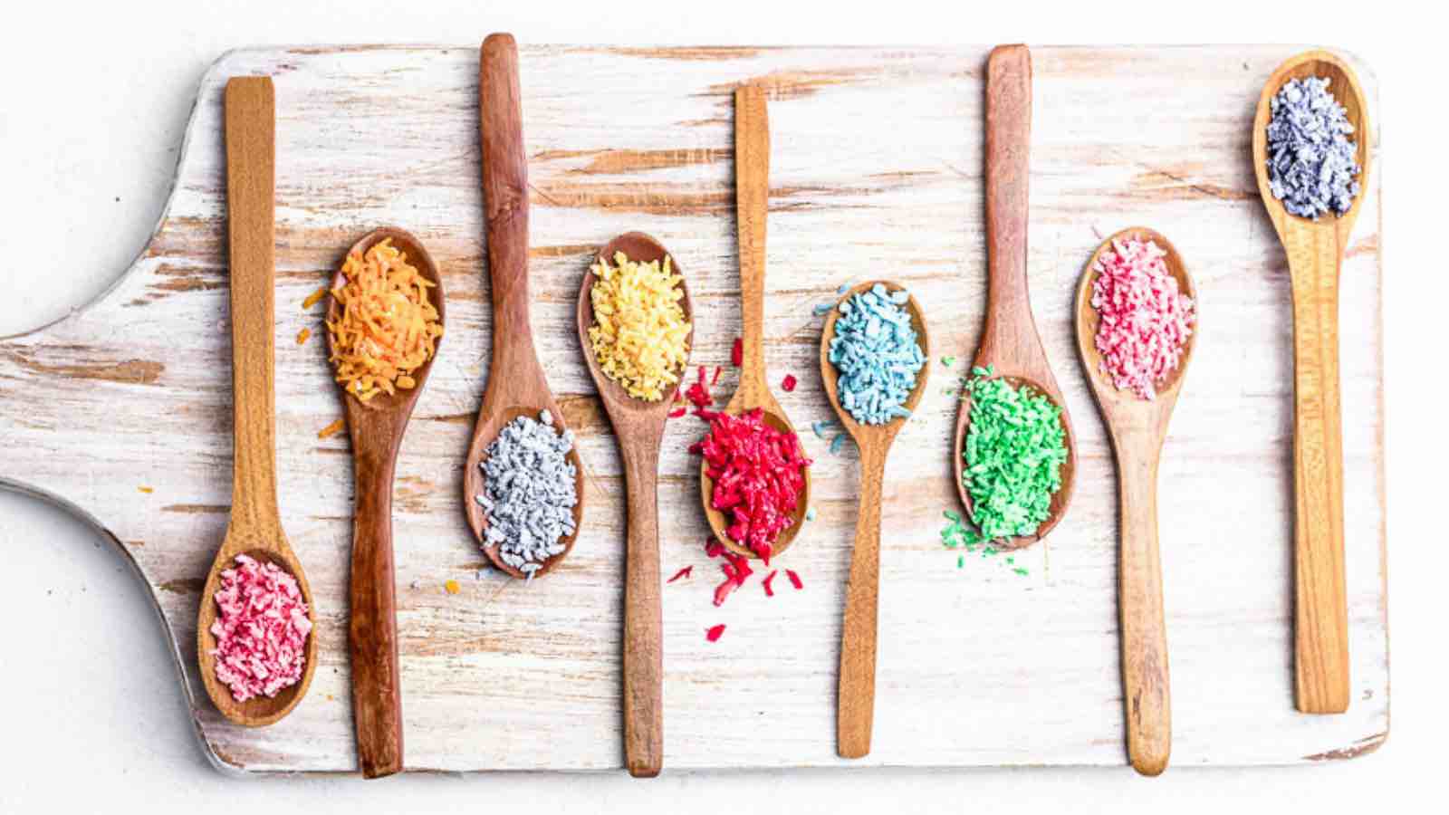 Colorful sprinkles in wooden spoons on a cutting board.