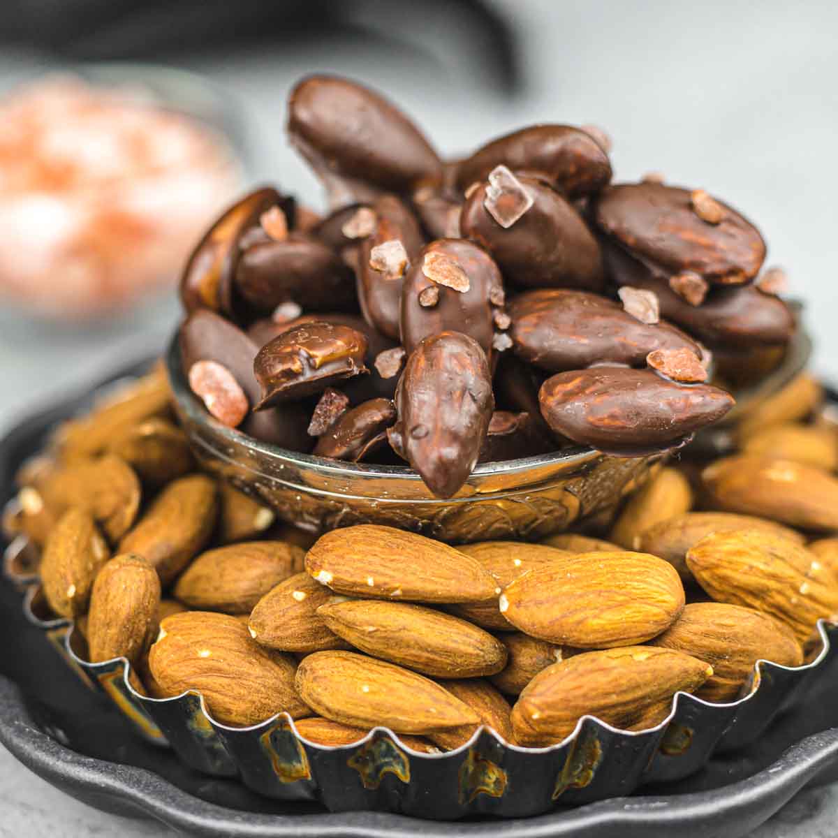 A plate of chocolate covered almonds on a black plate.