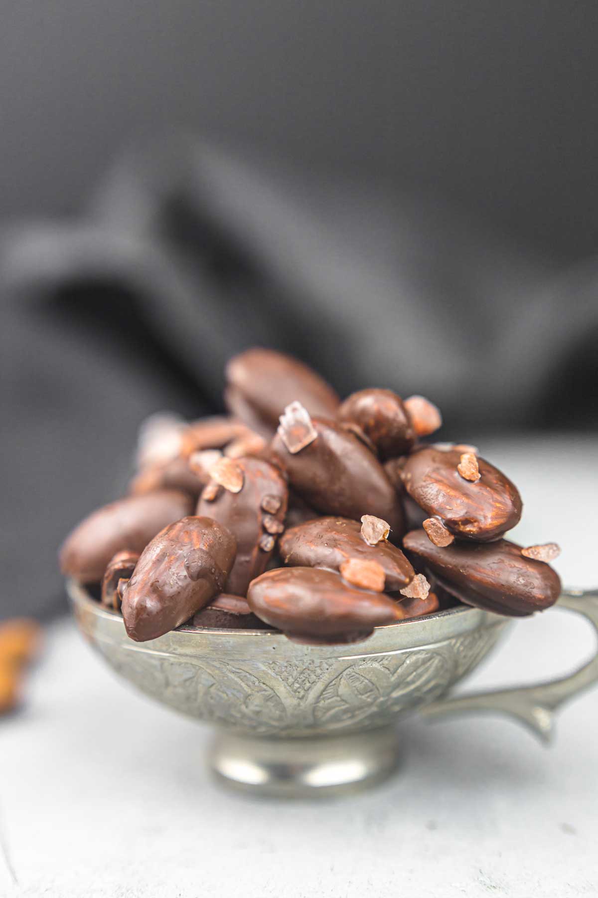 Chocolate covered almonds in a silver bowl.