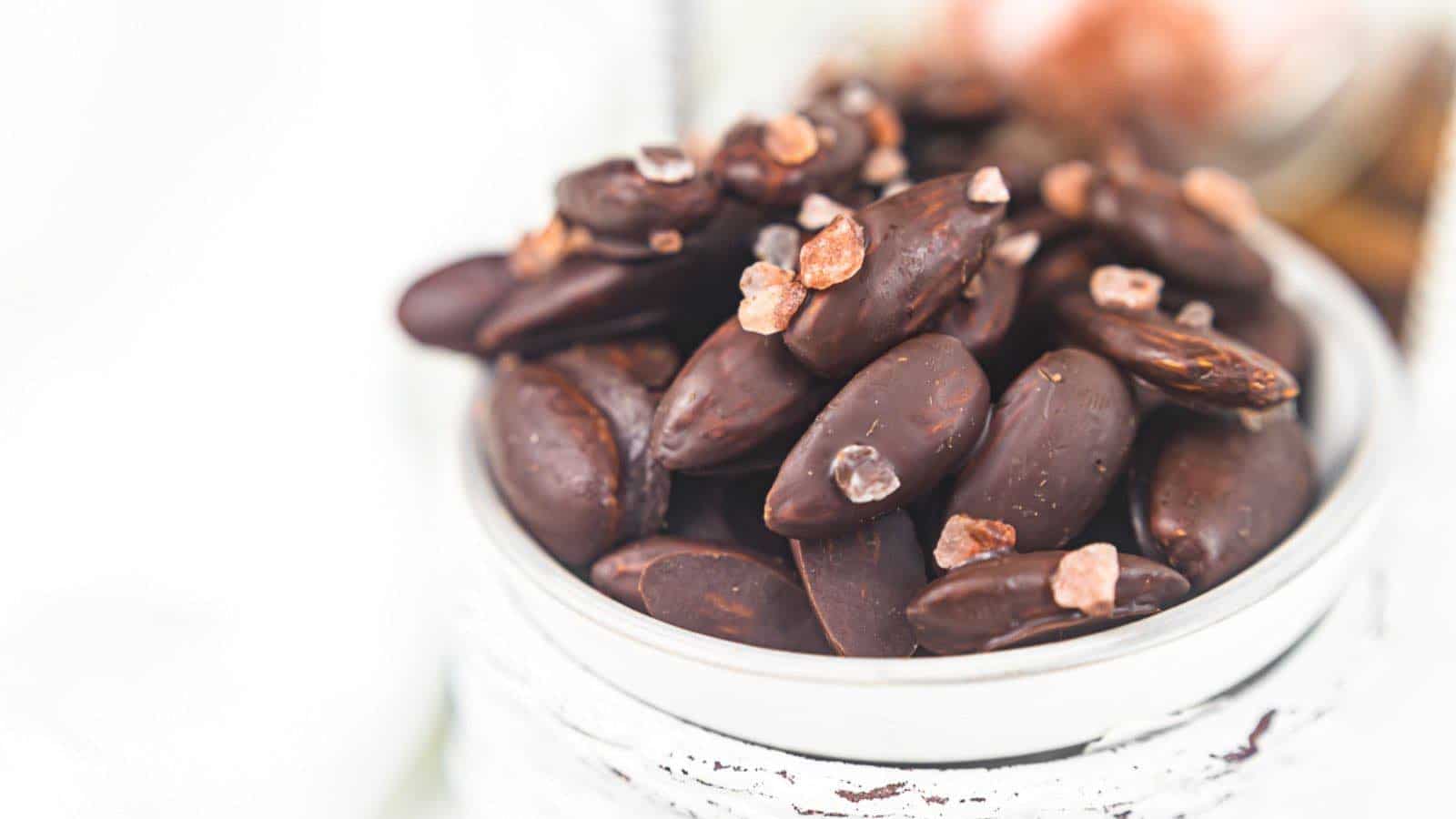Chocolate covered almonds in a jar on a white table.