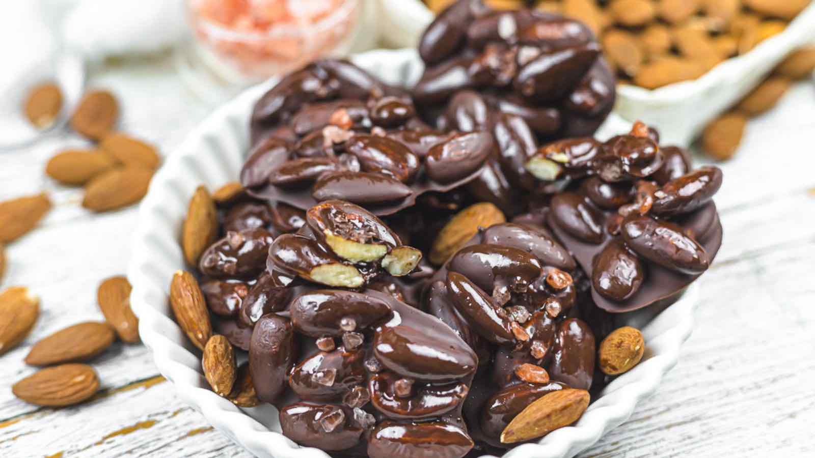 Chocolate covered almonds in a bowl on a wooden table.
