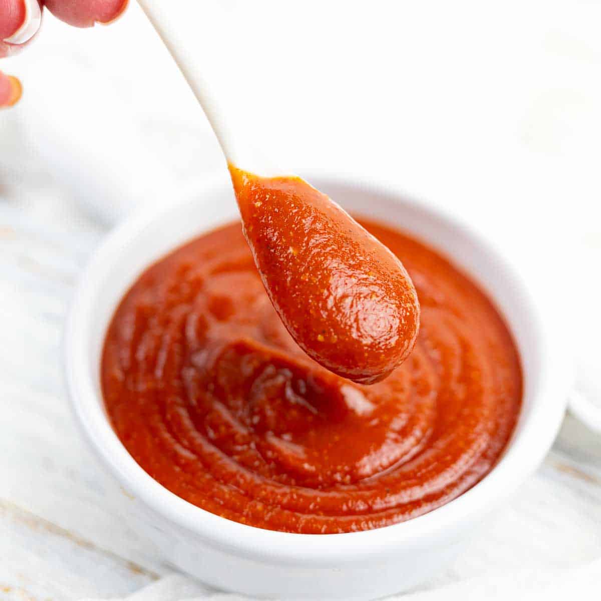 A person is dipping a spoon into a bowl of sauce.