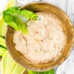 A bowl of creamy dip with herbs served with slices of green lettuce.