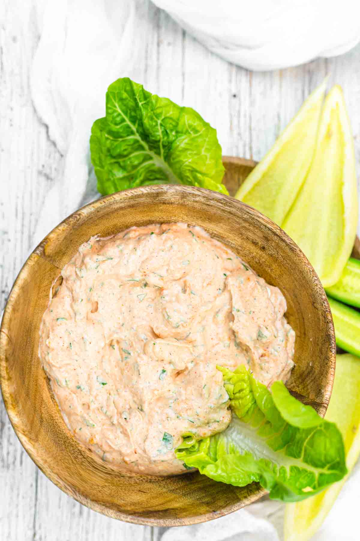 A bowl of creamy dip with herbs served with fresh lettuce on a wooden background.