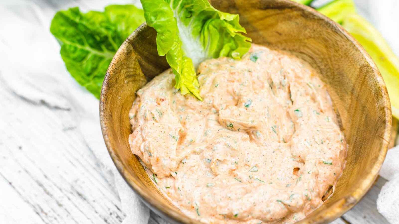 A bowl of creamy, herb-infused Buffalo Ranch dip garnished with a leaf of lettuce on a wooden surface.