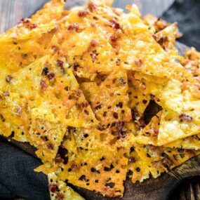 A festive pile of crispy, cheese-crusted nachos on a wooden serving board.