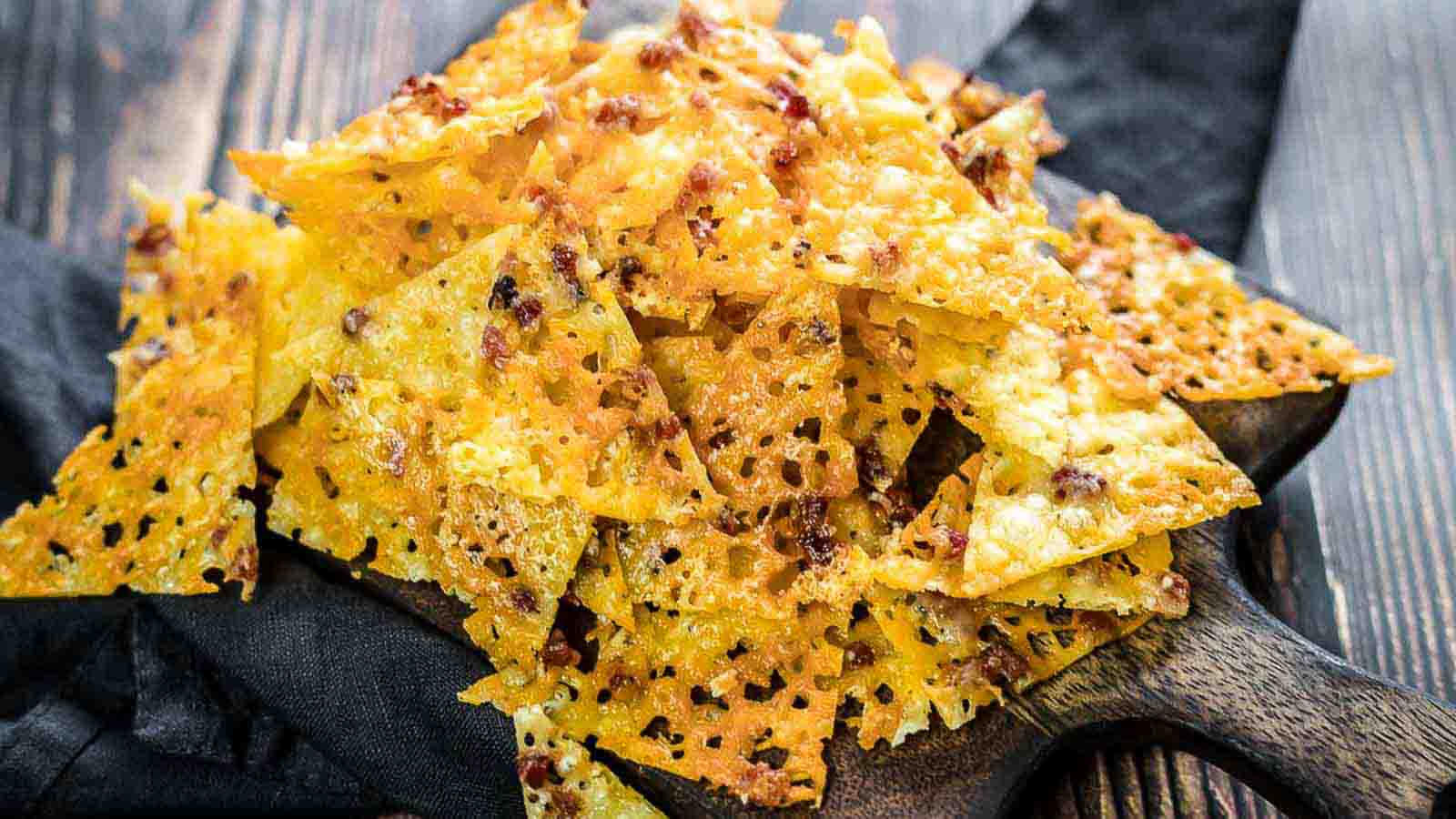 A festive pile of crispy, cheese-crusted nachos on a wooden serving board.
